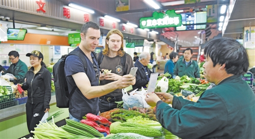4月14日，蒂姆（前左）领着朋友杰弗瑞（前左二）在杭州一家农贸市场购买蔬菜，并使用手机完成支付。来自澳大利亚悉尼的蒂姆，结缘一位杭州姑娘成了一名中国“洋女婿”，已在杭州定居生活了6年。 新华社记者 黄宗治摄